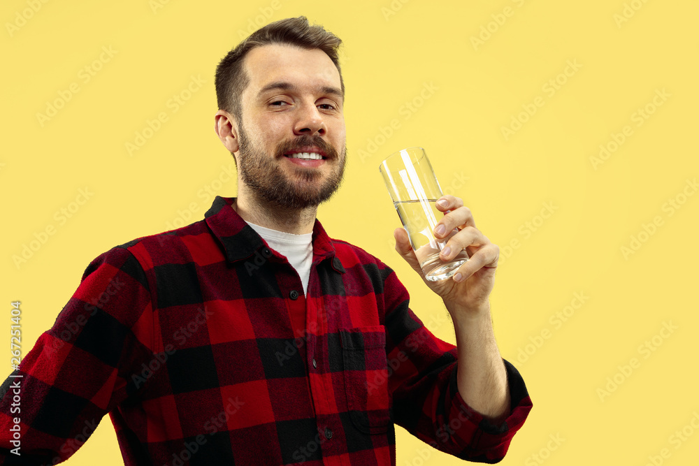 Half-length close up portrait of young man in shirt on yellow background. The human emotions, facial expression concept. Front view. Trendy colors. Negative space to insert your text. Drinking water. Half-length close up portrait of young man in shirt on yellow background. The human emotions, facial expression concept. Front view. Trendy colors. Negative space to insert your text. Drinking water.