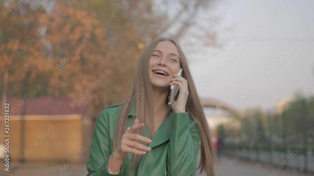 Girl with blond hair in a green jacket and blue eyes emotionally talking on the phone Girl with blond hair in a green jacket and blue eyes emotionally talking on the phone