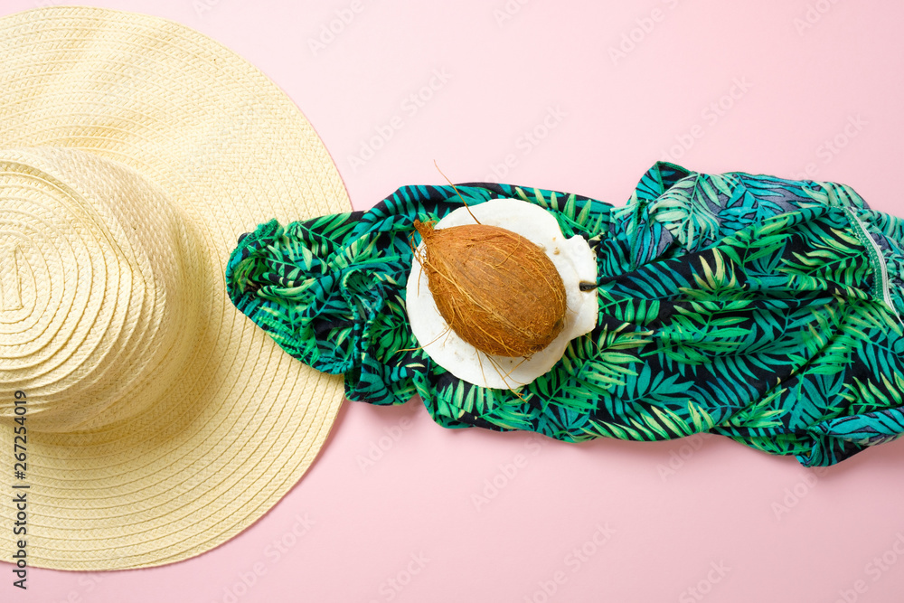 Creative layout with coconut, straw hat and green textile cloth on pink background. Tropical summer vacation concept. Top view, flat lay style composition