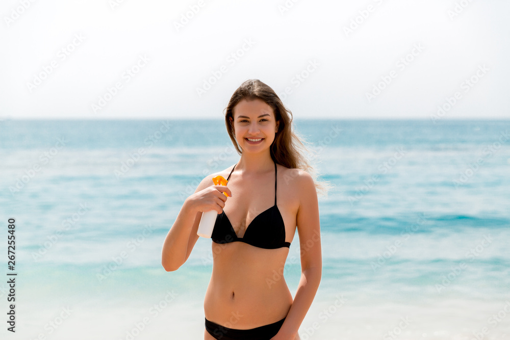Brown hair woman is applying sunsceen from the spray on her body at the sea background