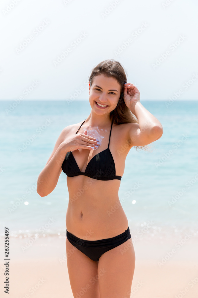 Young attractive woman is protecting her skin on the breast with sunblock at the sunny beach
