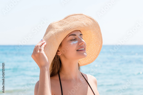 Foto Pretty woman protects her skin on face with sunblock at the beach
