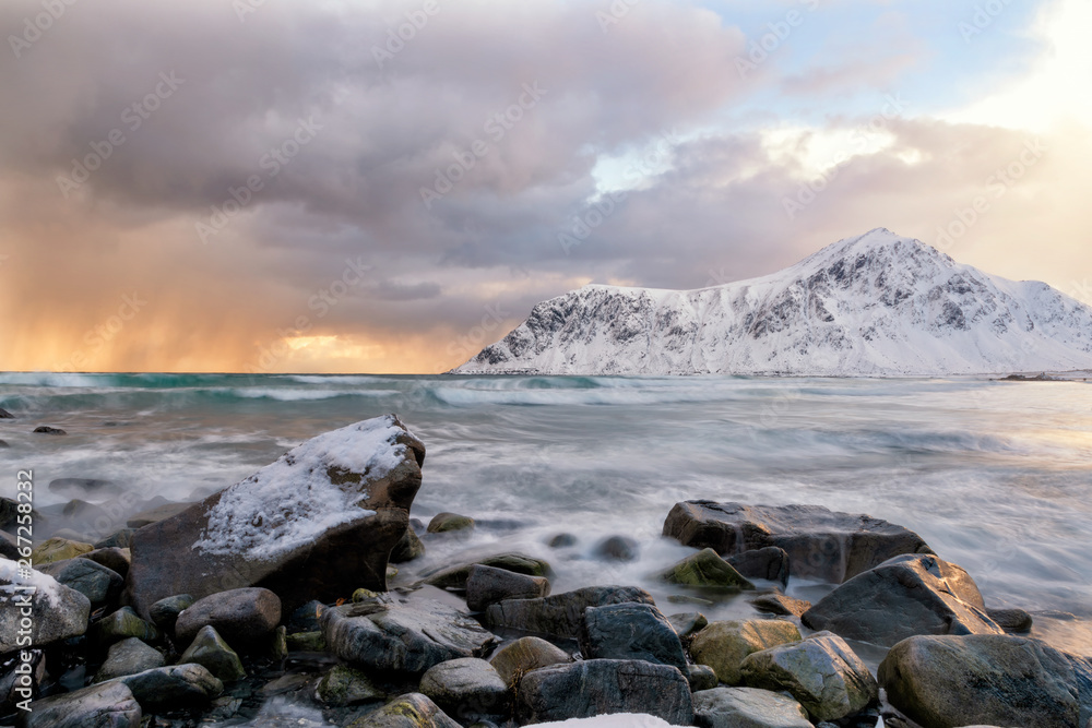 At sunset, strong waves, strong winds, rainy weather, storms are coming. At the beach area with black stones Behind the mountain There is snow covered throughout the area in lofoten norway.