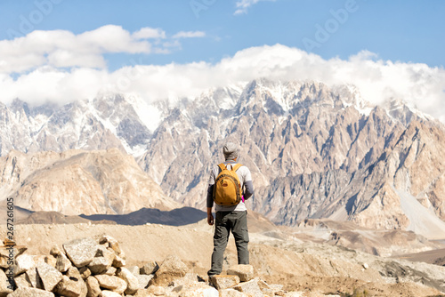 Asian men are tourists carrying backpacks, standing back, looking at the peak of passu on a clear day. During the autumn in hunza village in Pakistan