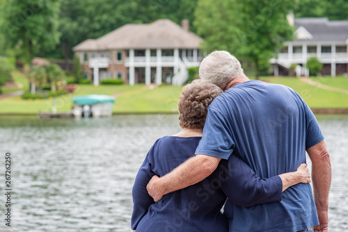 A beautiful senior couple contemplates the future, standing together on a dock, overlooking a beautiful, scenic lake.