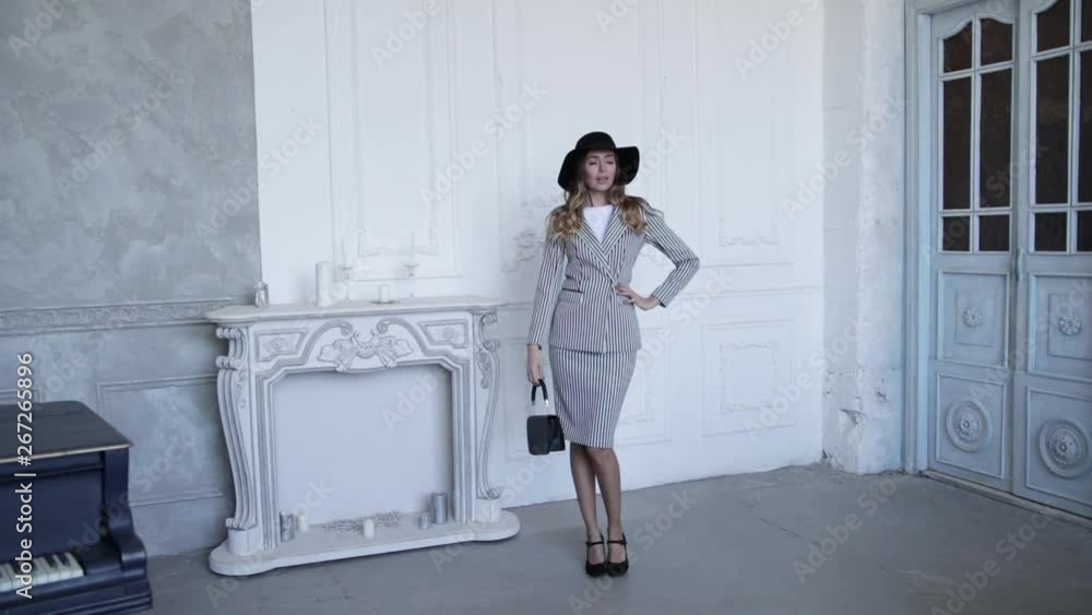 Gorgeous girl on the background of the fireplace, posing in a black hat with a bag and striped jacket and trousers . Slow motion Gorgeous girl on the background of the fireplace, posing in a black hat with a bag and striped jacket and trousers . Slow motion