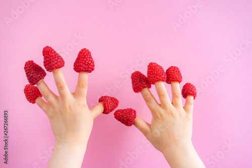 Little girl hands with raspberries on fingers in pink background, copy space. Summer creative concept