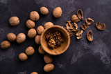 Cracked walnuts in wooden bowl and on black slate surface. Healthy nuts and seeds composition.