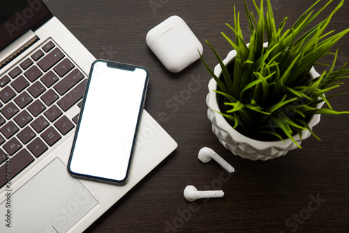 Top view on a smartphone laptop keyboard and wireless headphones on a brown table next to a houseplant photo