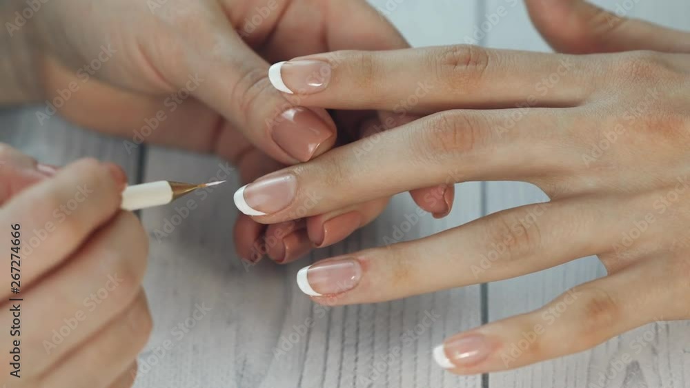 the manicurist paints the client's nails with nail polish on a white background Painting nails. Female hands with beautiful french manicure the manicurist paints the client's nails with nail polish on a white background Painting nails. Female hands with beautiful french manicure