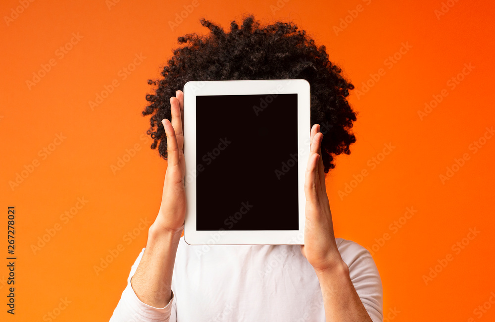 Young man hiding his face behind digital tablet - obrazy, fototapety, plakaty 