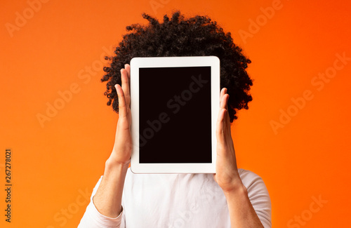 Young man hiding his face behind digital tablet
