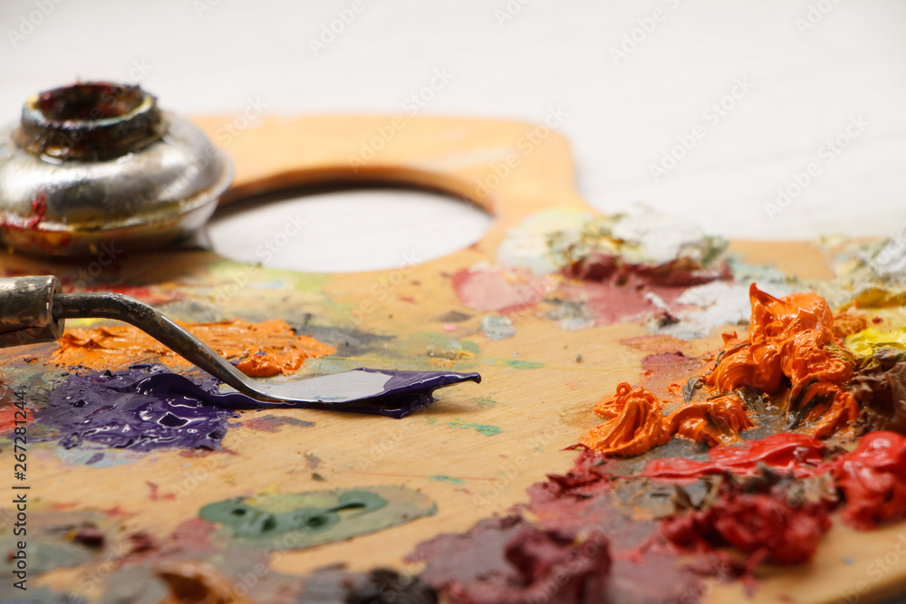 Closeup of palette with colorful paints and spatula on white surface, background Closeup of palette with colorful paints and spatula on white surface, background