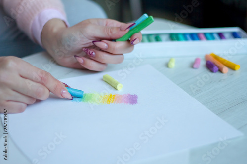 Close-up of female hands are drawing with multicolored chalks on a white sheet, a box with crayons