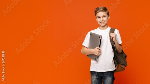 Friendly schoolboy holding laptop, going to school with computer photo