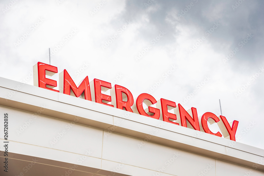 A prominent red 3D all-caps lighted emergency directional sign and marker perched on the awning and canopy of the main hospital entrance. A prominent red 3D all-caps lighted emergency directional sign and marker perched on the awning and canopy of the main hospital entrance.