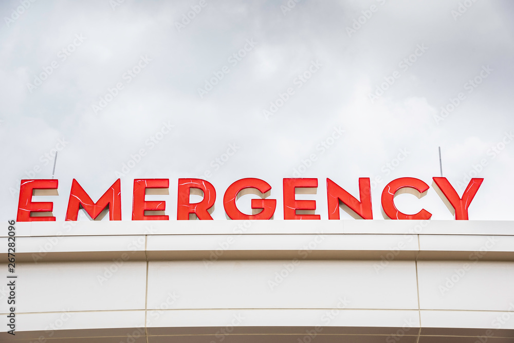 A prominent red 3D all-caps lighted emergency directional sign and marker perched on the awning and canopy of the main hospital entrance. A prominent red 3D all-caps lighted emergency directional sign and marker perched on the awning and canopy of the main hospital entrance.