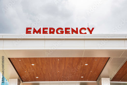 A prominent red 3D all-caps lighted emergency directional sign and marker perched on the awning and canopy of the main hospital entrance.