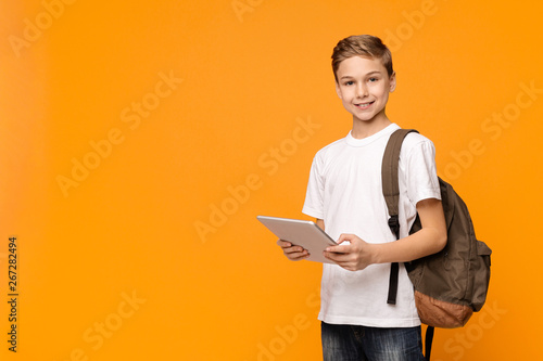 Schoolboy with backpack using tablet computer and smiling