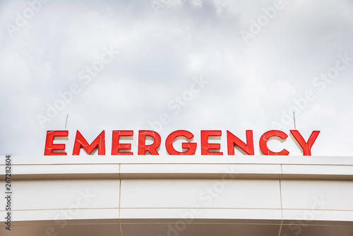 A prominent red 3D all-caps lighted emergency directional sign and marker perched on the awning and canopy of the main hospital entrance.