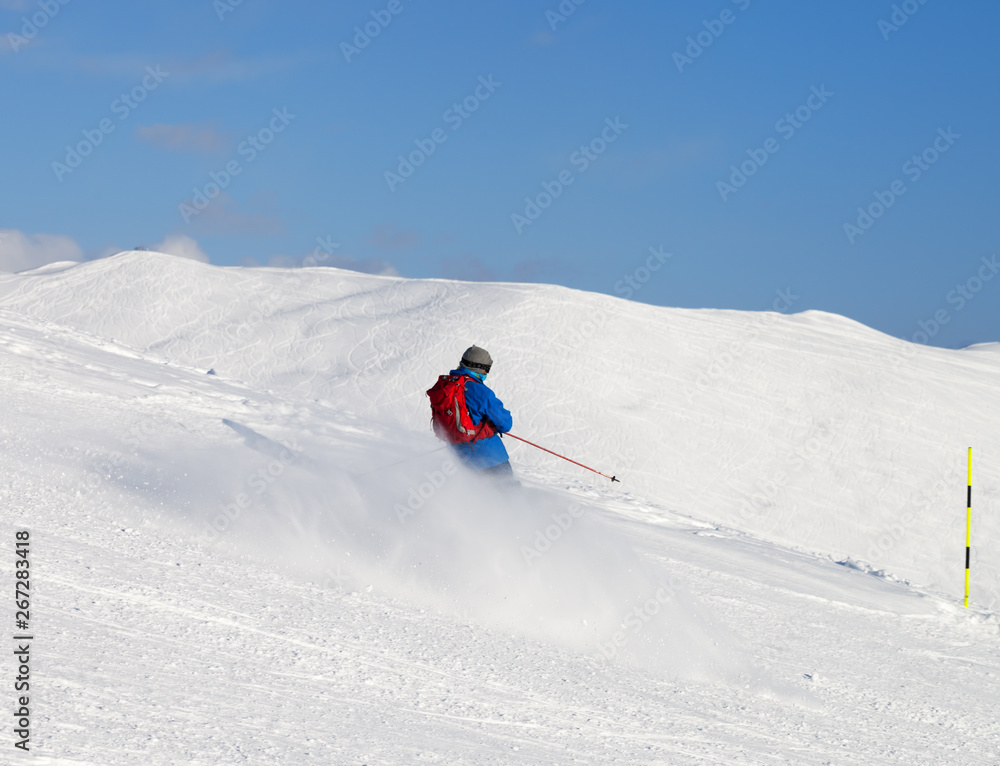 Skier downhill on snowy ski slope in sunny winter day