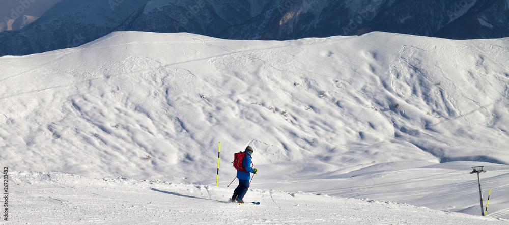 Skier downhill on snowy ski slope in sun winter evening