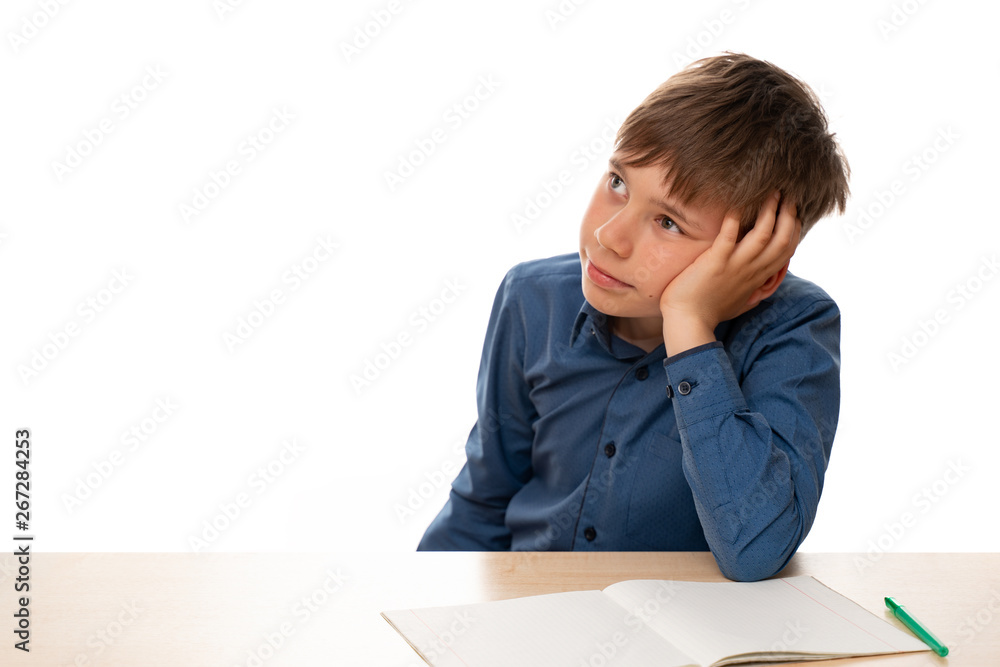 The child is sitting at the desk and dreams about something, instead of doing his homework. Portrait of a child, isolated, on a white background. The child is sitting at the desk and dreams about something, instead of doing his homework. Portrait of a child, isolated, on a white background.