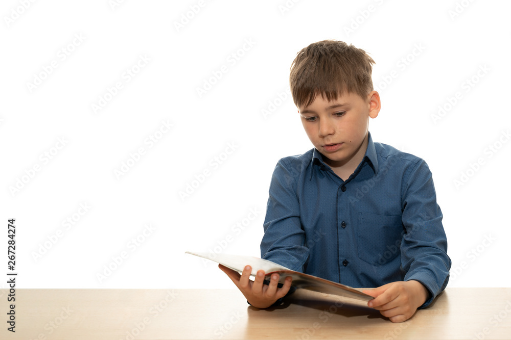 The child sits at the table and carefully reads the notes in the notebook. Baby portrait isolated on white background. Copy space The child sits at the table and carefully reads the notes in the notebook. Baby portrait isolated on white background. Copy space