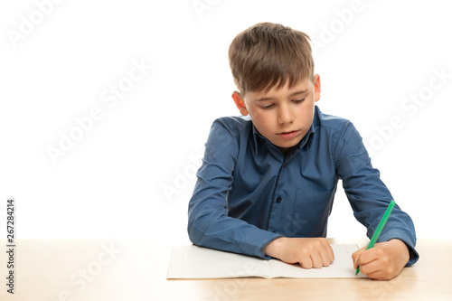 Konstfotografi A left-handed child in a blue shirt, on a white isolated background, sits at the table and writes in his left hand