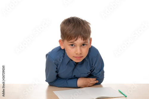 The schoolboy is sitting at the table and peering intently from the photo. Portrait of a child isolated on a white background.