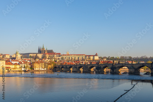 Outdoor sunny view of Charles Bridge, Prague Castle, St. Vitus Cathedral and riverside of Vltava River in Prague, Czech Republic in the morning with blue sunrise sky and daybreak atmosphere.