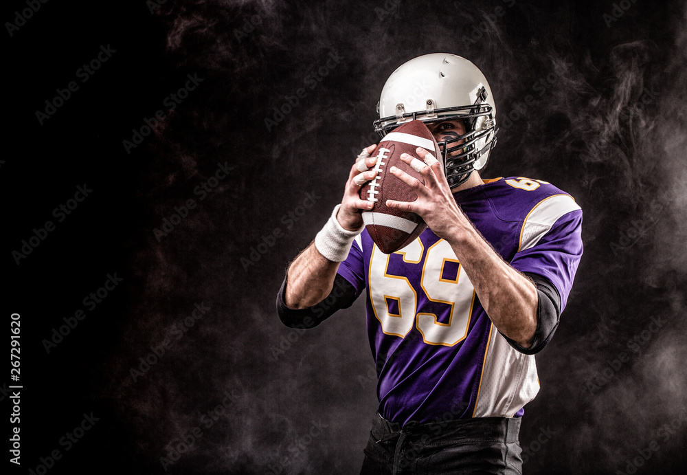 American football player holding ball in his hands in smoke. Black background, copy space. The concept of American football, motivation, copy space