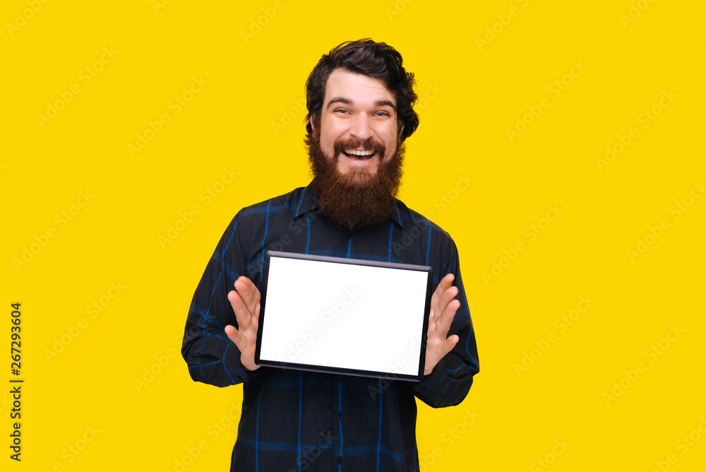Cheerful bearded guy holding a tablet, and showing white screen blank, over yellow background Cheerful bearded guy holding a tablet, and showing white screen blank, over yellow background
