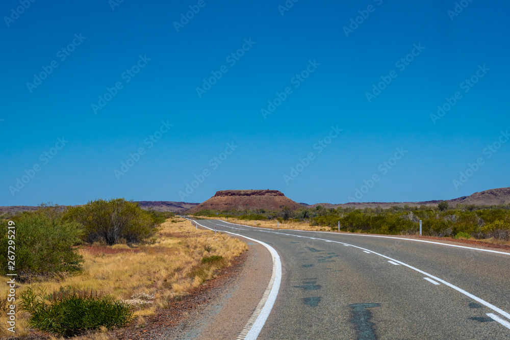 Hill behind empty road in Western Australia leading towards Karijini National Park