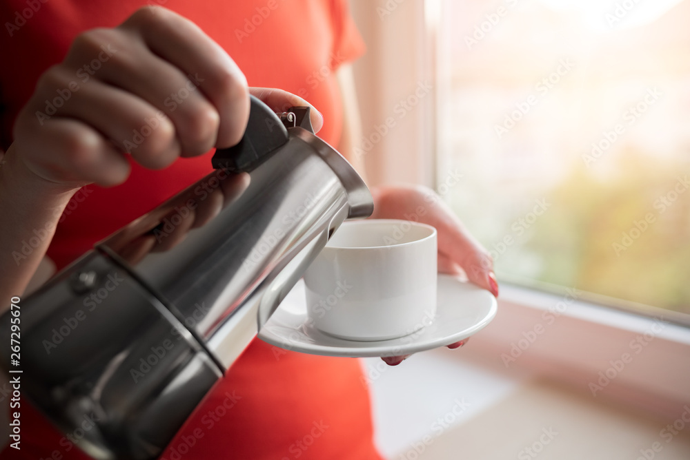 Fototapeta premium A woman pours coffee into a cup from a coffee maker.
