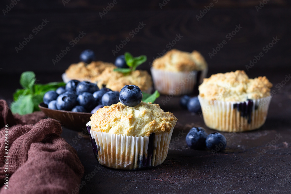 Blueberry muffins with fresh berries and mint leaves on dark brown stone background. Copy space.