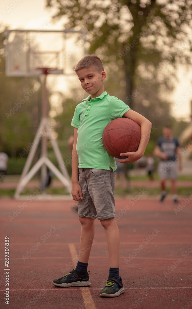one little boy posing, holding a basketball ball, on a basketball court.