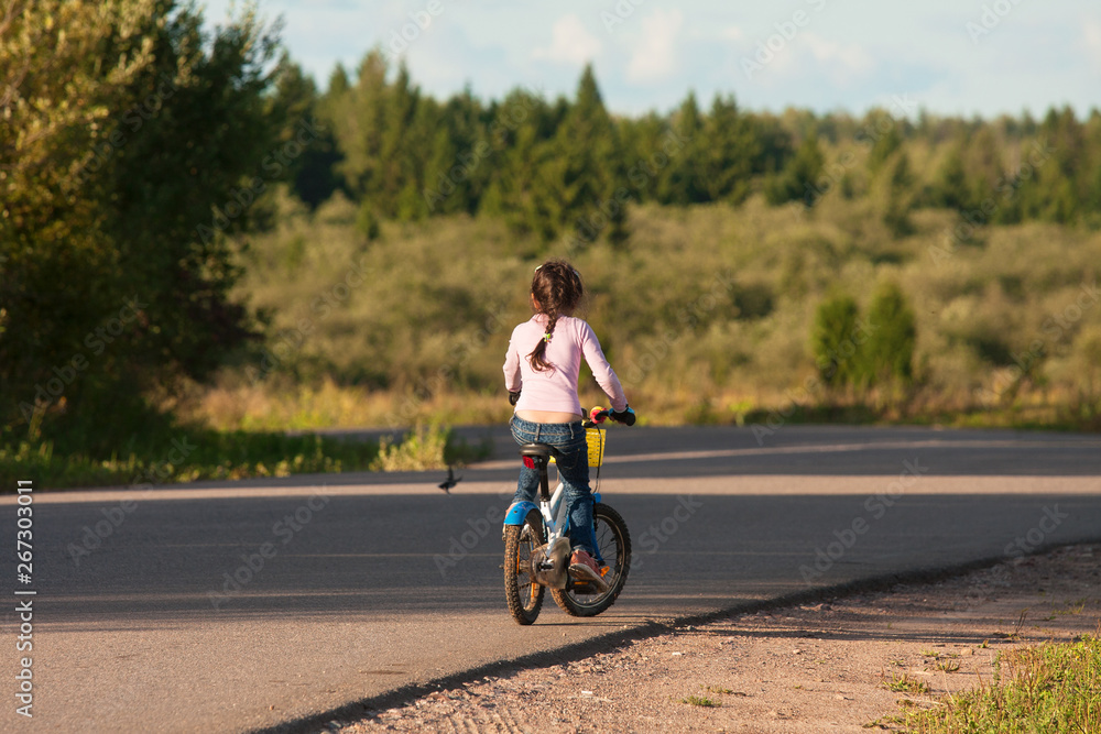 Little girl, dressed in jeans, rides a bike facing away from the camera. Little girl, dressed in jeans, rides a bike facing away from the camera.