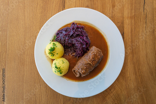 Fotografia Rinderroulade, Beef roll or roulades, traditional german meal, thin meat wrap bacon, onion and pickle, serve with pickled red cabbage, dumplings potatoes and sauce on white plate and wooden table