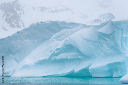 Beautiful turquoise blue iceberg floating in the Antarctic, against a foggy background