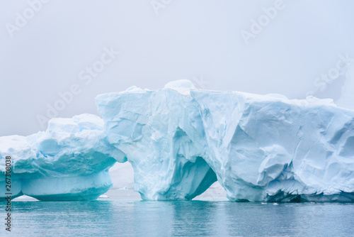 Beautiful turquoise blue iceberg floating in the Antarctic  against a foggy background