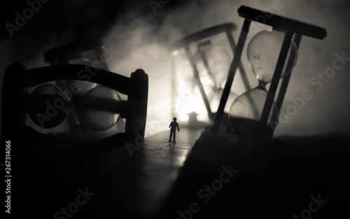 Time concept. Silhouette of a man standing between hourglasses with smoke and lights on a dark background. Surreal decorated picture