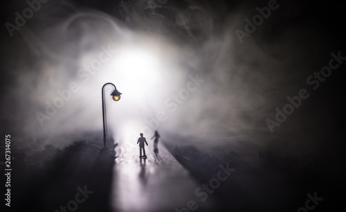 Fototapeta Naklejka Na Ścianę i Meble -  Young couple holding each other hands. Slowly walking under white street lights in night. Dark time. Peaceful atmosphere in mist. Foggy air.