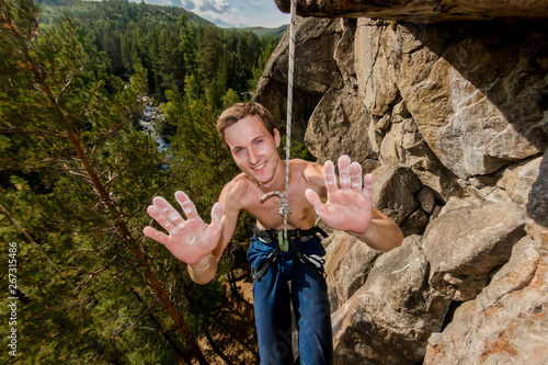 Extreme climber hanging on a rope and showing hands palm in magnesia, portrait smiling