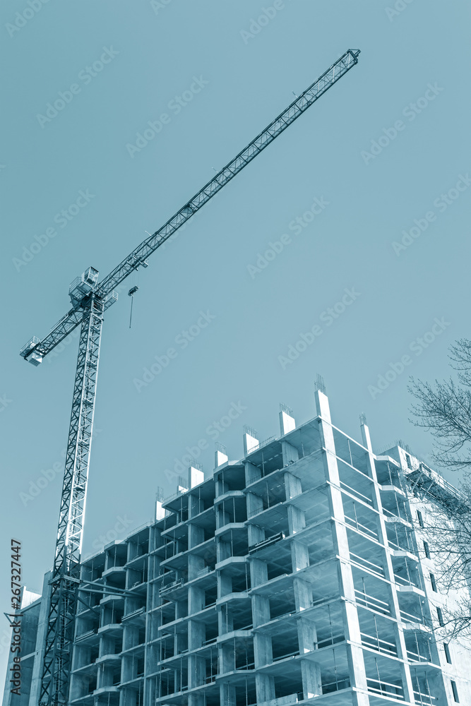 tower crane near apartment building under construction against blue sky background