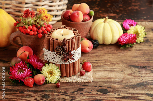 Candle decorated with cinnamon sticks among autumn fruits and flowers.