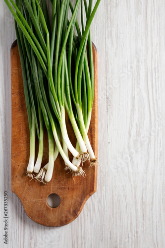 Fresh green onions on a cutting board on a white wooden table, top view. From above, overhead, flat lay. Copy space.