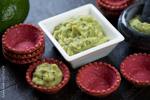 Bowl of freshly made guacamole with vegetable tartlets, close-up, studio shot