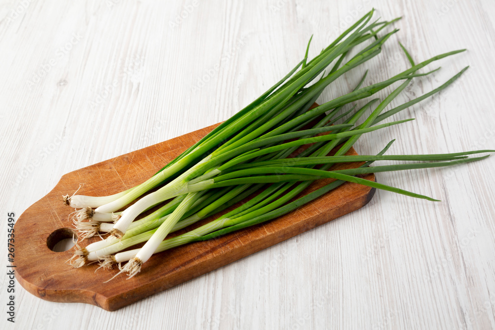 Fresh green onions on a cutting board over white wooden background, side view. Close-up. Fresh green onions on a cutting board over white wooden background, side view. Close-up.