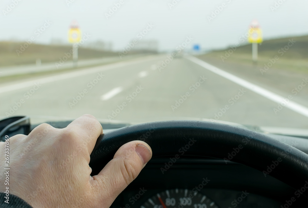 View of the driver's hand on the steering wheel of the car that is driving on the highway